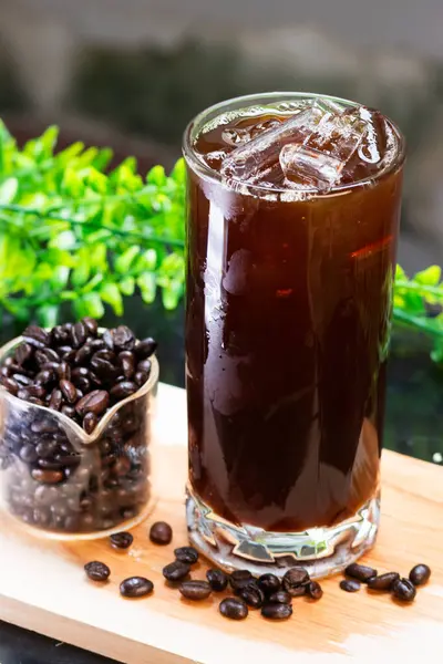 Uzun bir bardakta, buzlu, ferahlatıcı bir kahve. Yanında da tahtanın üzerinde kavrulmuş kahve çekirdekleri servis ediliyor..