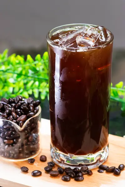 Uzun bir bardakta, buzlu, ferahlatıcı bir kahve. Yanında da tahtanın üzerinde kavrulmuş kahve çekirdekleri servis ediliyor..