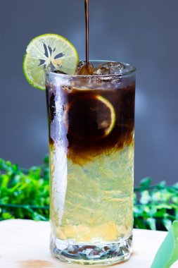 Uzun bardakta buzlu limonlu kahve, narenciye katmanlı espresso, limon dilimi garnitür ve buz ile servis edilir..