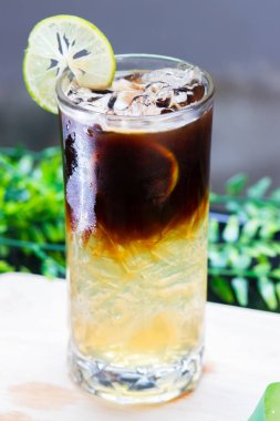 Uzun bardakta buzlu limonlu kahve, narenciye katmanlı espresso, limon dilimi garnitür ve buz ile servis edilir..