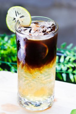 Uzun bardakta buzlu limonlu kahve, narenciye katmanlı espresso, limon dilimi garnitür ve buz ile servis edilir..