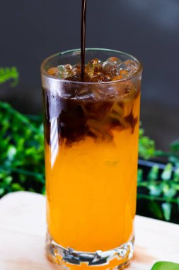 Uzun bir bardakta buzlu portakal kahvesi, parlak portakal suyunun üzerine espresso katılmış, ferahlatıcı bir içecek için buz küpleriyle servis edilmiş..