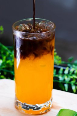 Uzun bir bardakta buzlu portakal kahvesi, parlak portakal suyunun üzerine espresso katılmış, ferahlatıcı bir içecek için buz küpleriyle servis edilmiş..