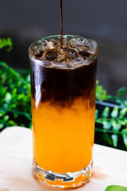 Uzun bir bardakta buzlu portakal kahvesi, parlak portakal suyunun üzerine espresso katılmış, ferahlatıcı bir içecek için buz küpleriyle servis edilmiş..