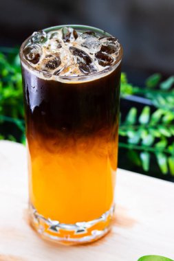 Uzun bir bardakta buzlu portakal kahvesi, parlak portakal suyunun üzerine espresso katılmış, ferahlatıcı bir içecek için buz küpleriyle servis edilmiş..