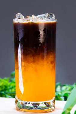 Uzun bir bardakta buzlu portakal kahvesi, parlak portakal suyunun üzerine espresso katılmış, ferahlatıcı bir içecek için buz küpleriyle servis edilmiş..