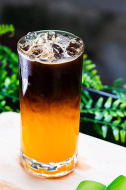 Uzun bir bardakta buzlu portakal kahvesi, parlak portakal suyunun üzerine espresso katılmış, ferahlatıcı bir içecek için buz küpleriyle servis edilmiş..