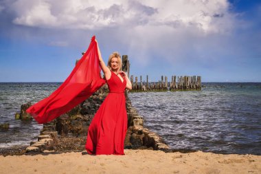 Kumsalda sarışın bir kadınla ilginç bir tatil konsepti. Gdynia, Polonya 'da Baltık Denizi kıyısında kırmızı elbiseli güzel bir kadın..