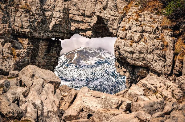 Interesting concept with a rock window overlooking the white snowy peaks. Window rock in mountains alps in Austria.