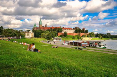 Krakow, Polonya - 16 Ağustos 2014: Wawel Kraliyet Kalesi, Krakow. Çayırlarda turistler ve Vistula Nehri 'nde tekneler ve güneşli yaz gününde arka planda Wawel Royal Castle, Polonya.