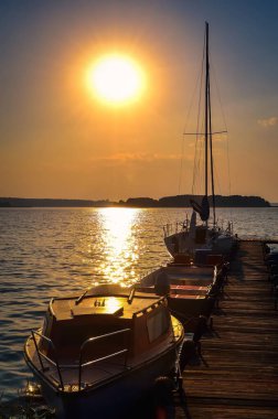 Güzel gölde yelkenli ve iskele. Polonya 'nın Mazury bölgesinde güneş doğarken, göl kıyısında demirli tekneleri olan boş ahşap iskele..