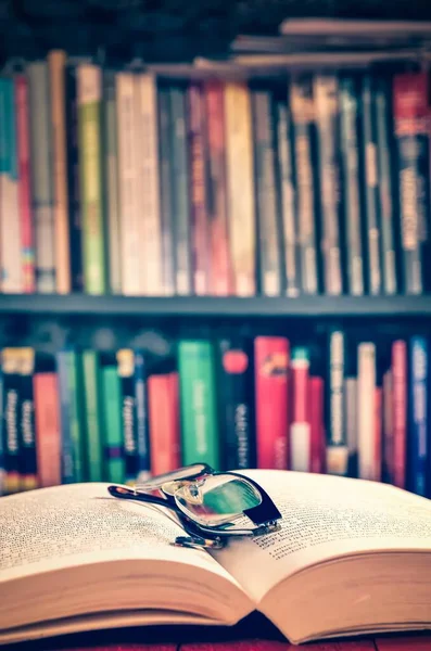 Open book and glasses with books on a shelf in the background. Theme of spending free time deepening your knowledge. Photo with a shallow depth of field.