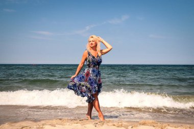 Güneşli bir günde sahilde kadınsı bir seans. Polonya Baltık Denizi kıyısında sarı saçlı ve renkli elbiseli bir kız..