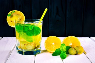 Beyaz ahşap bir masa üzerinde bir bardak içki. Limon, zencefil ve nane ile iç.