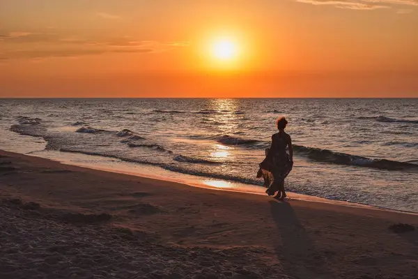 Deniz kenarında güzel bir akşam manzarası olan bir kadın. Arka planda batan güneşle sahilde yürüyen kız. Fotoğraf Leba, Polonya 'da Baltık Denizi' nde çekildi..