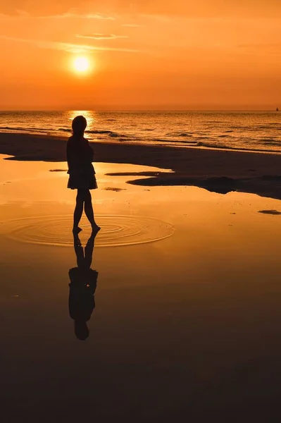 Woman on the seashore in a beautiful evening scenery. Girl walking on the beach with the setting sun in the background. Photo taken at the Baltic Sea in Leba, Poland.