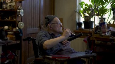 Elderly male master works in his workshop restoring japanese sword sheath