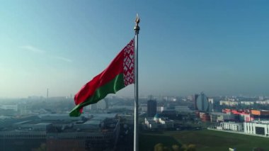 Beyaz Rusya bayrağı açık mavi gökyüzü ve güneşli bir sabahta Minsk şehri üzerinde dalgalanıyor.
