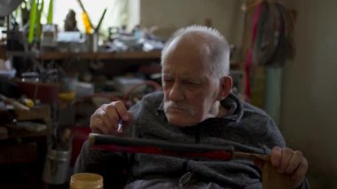 Elderly male master works in his workshop restoring japanese sword sheath