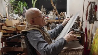 Tekerlekli sandalyedeki yaşlı kuyumcu bir atölyede çalışıyor.