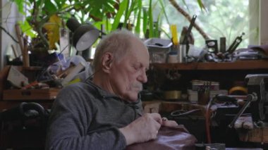 Tekerlekli sandalyedeki yaşlı kuyumcu bir atölyede çalışıyor.