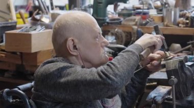 Tekerlekli sandalyedeki kıdemli yaşlı kuyumcu bir atölyede çalışıyor.