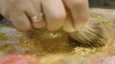 Ressam, tuvaldeki yağlı boya resme altın uygular.