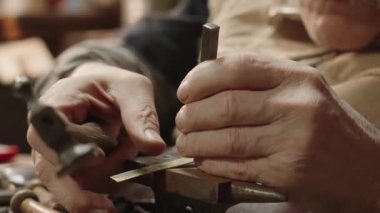 Senior elderly master jeweler in wheelchair works in a workshop with an anvil