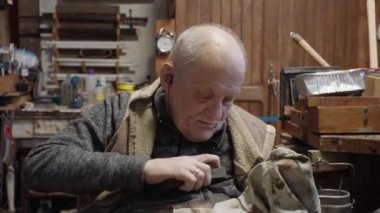 Senior gray haired male master in a wheelchair is working at his workshop sharpening japanese swords blade