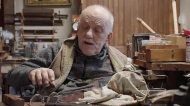 Senior gray haired male master in a wheelchair is working at his workshop sharpening japanese swords blade