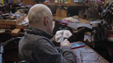 Senior gray haired male master in a wheelchair is working at his workshop sharpening japanese swords blade