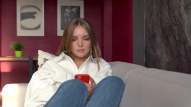 Evdeki kanepede akıllı telefon kullanan genç bir kadın.