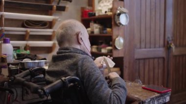 Senior gray haired male master in a wheelchair is working at his workshop sharpening japanese swords blade