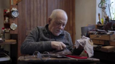 Senior gray haired male master in a wheelchair is working at his workshop sharpening japanese swords blade