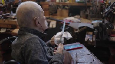 Senior gray haired male master in a wheelchair is working at his workshop sharpening japanese swords blade