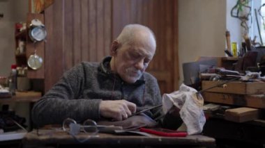 Senior gray haired male master in a wheelchair is working at his workshop sharpening japanese swords blade