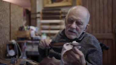 Senior gray haired male master in a wheelchair is working at his workshop sharpening japanese swords blade