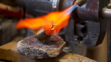 Craftsman soldering the metal tip of the scabbard in the workshop