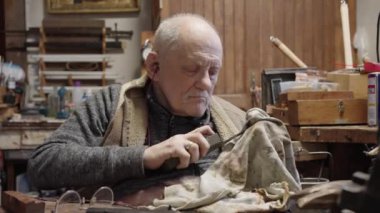 Senior gray haired male master in a wheelchair is working at his workshop sharpening japanese swords blade