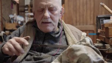 Senior gray haired male master in a wheelchair is working at his workshop sharpening japanese swords blade