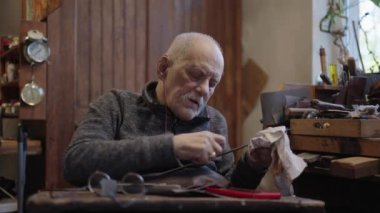Senior gray haired male master in a wheelchair is working at his workshop sharpening japanese swords blade