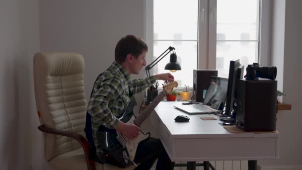 昼間机の上の部屋でエレキギターを弾いている若者 — ストック動画