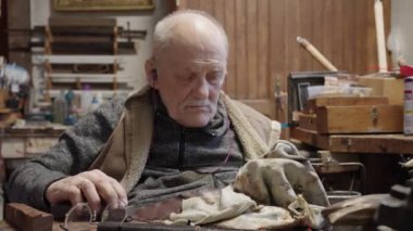 Senior gray haired male master in a wheelchair is working at his workshop sharpening japanese swords blade