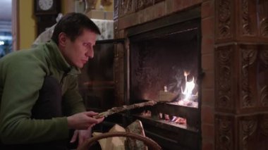 Evdeki şömineye odun koyan bir adam ateş yakıyor.
