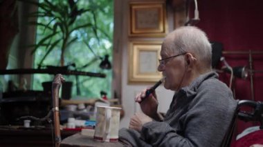 Tekerlekli sandalyedeki yaşlı bir adam yatak odasındaki yatağın yanında ilaç alıyor.