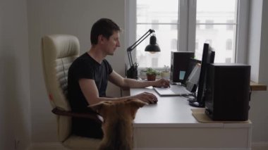 Genç bir adam evdeki masasının yanında bir köpekle video görüşmesi yapıyor. Uzak bir çevrimiçi çalışma konsepti.