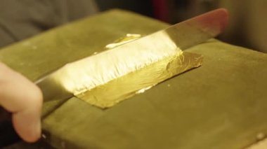 Ressam, yağlı boya resme uygulamak için özel bir bıçakla altın yaprak kesiyor.