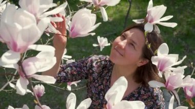 Mutlu kadın doğanın tadını çıkarıyor ve güneşli bir günde bahçede çiçek açan manolyaya dokunuyor.