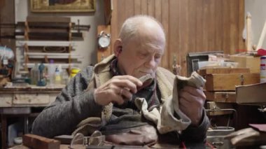 Senior gray haired male master in a wheelchair is working at his workshop sharpening japanese swords blade
