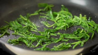 Şef tavada taze kesilmiş ıspanak pişiriyor.